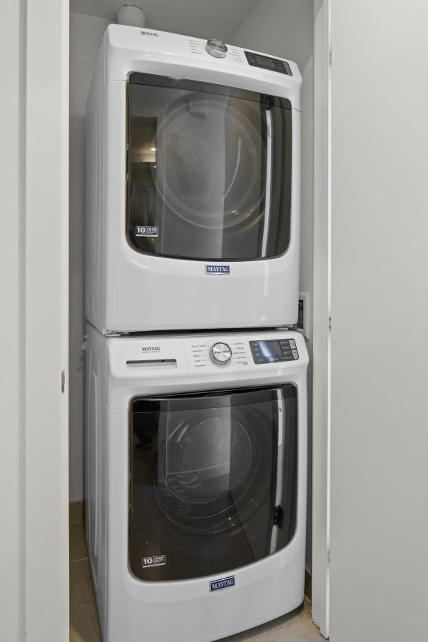 A stacked Maytag washer and dryer set is installed in a small, white laundry closet with closed doors on either side.