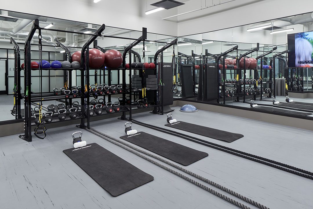 Modern gym with exercise mats, kettlebells, battle ropes, medicine balls, resistance bands, and dumbbells in front of mirrored walls. The space is clean, organized, and well-lit, with a TV on the right wall.