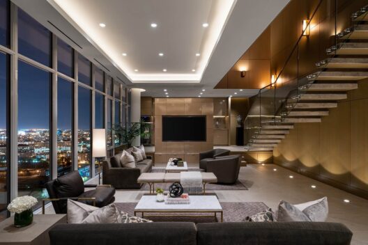 Modern, luxurious living room at night with floor-to-ceiling windows showing a cityscape, contemporary furniture, a large TV, decorative objects, and a floating staircase along a wood-paneled wall with recessed lighting.