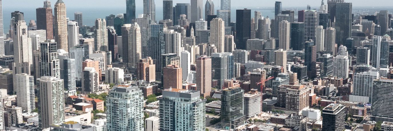 Aerial view of a dense urban cityscape with numerous high-rise buildings, skyscrapers, and an expanse of modern architecture under a clear sky.