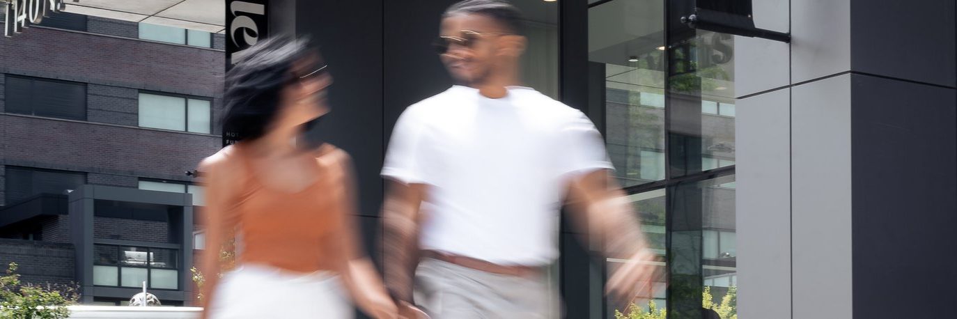 A blurred image of a couple holding hands and walking outdoors in an urban area with modern buildings in the background.