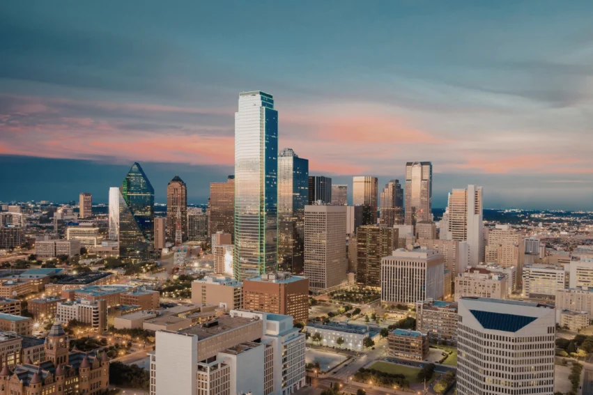 Aerial view of a city skyline at sunset, featuring tall modern skyscrapers, illuminated buildings, and a mix of architectural styles under a partly cloudy sky.